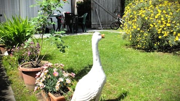 A white bird statue in a garden with potted plants and a wooden fence in the background.