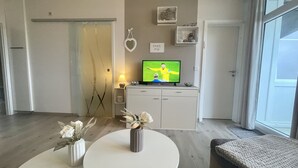 Un salon moderne avec un téléviseur, une table ronde et deux vases ornés de fleurs.
