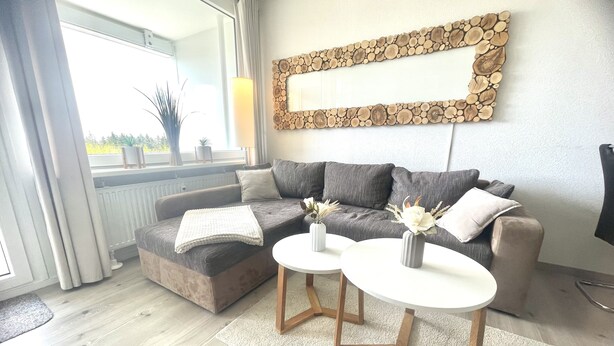 Un salon moderne avec un canapé gris, deux tables basses blanches et un élément décoratif mural en forme de bûche.