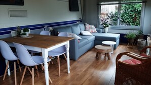 Ein modernes Wohnzimmer mit Esstisch aus Holz, blauem Sofa und Korbstuhl.