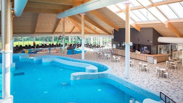 Ein Innenpool mit gefliestem Boden, umgeben von Liegestühlen und einer Bar.