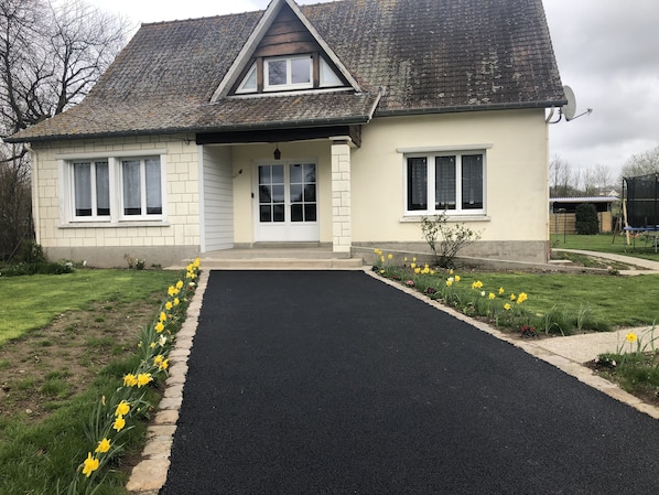 A two-story house with a sloped roof, a front porch, and a driveway leading to the entrance. - Gite des 3 Pleureuses (ST RIQUIER)