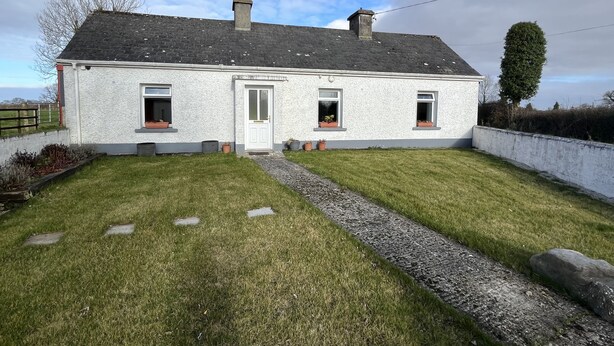 Une maison à deux étages, avec une façade blanche, un toit gris et un petit jardin à l’avant.