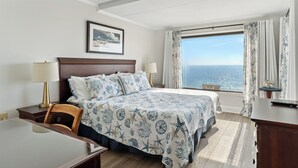 Una habitación de hotel con una cama grande, dos mesitas de noche, un escritorio y vista al océano.