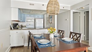 Un comedor con una mesa de madera dispuesta para cuatro, individuales azules y un florero con flores amarillas.