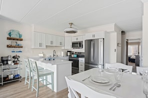 A modern kitchen with white cabinetry, a central island, stainless steel appliances, and a dining area with a white table set for four.