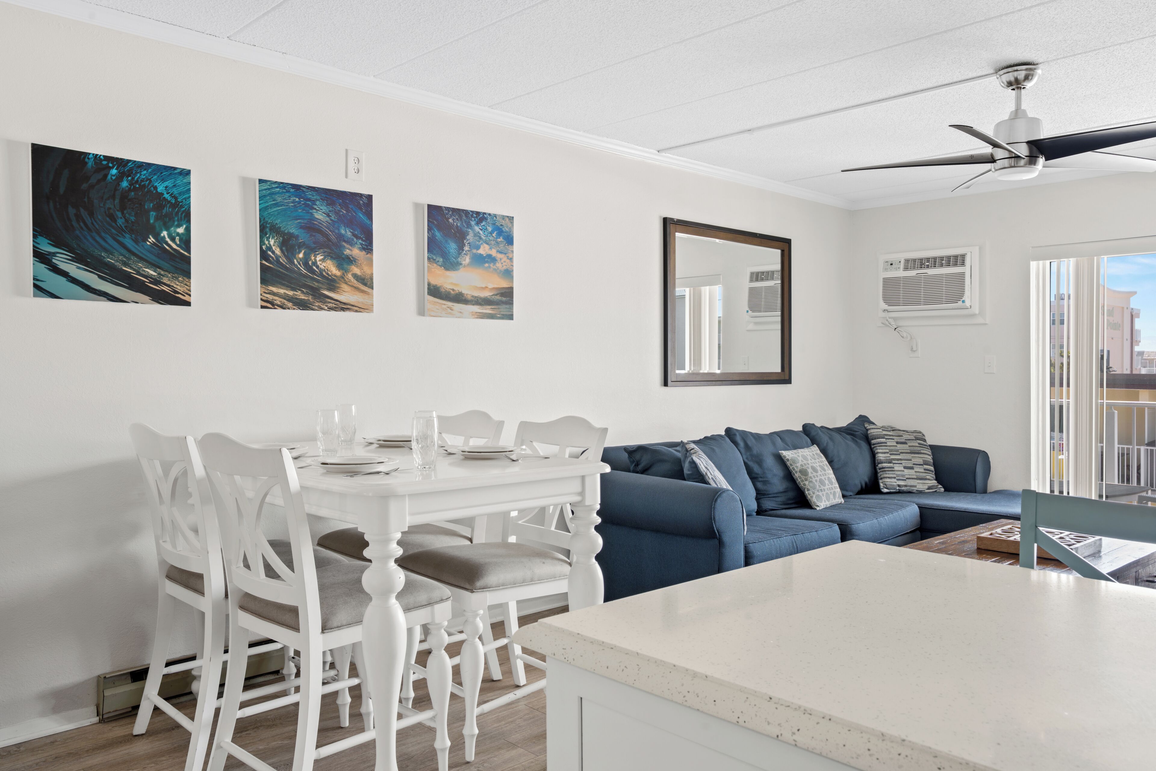 Ein modernes Wohnzimmer mit Essbereich, einem blauen Sofa, weißen Esszimmerstühlen und Kunstwerken an der Wand.