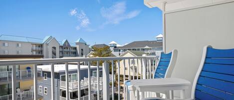 A balcony with a white table and blue chairs, overlooking a residential area with multi-story buildings.