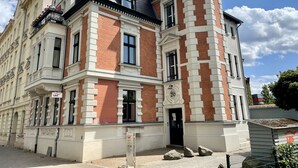 Um edifício histórico com entrada na esquina, telhado preto e uma mistura de tijolos vermelhos e brancos.
