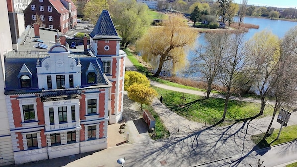 A historic building with a tower, a paved pathway, and a lake in the background.