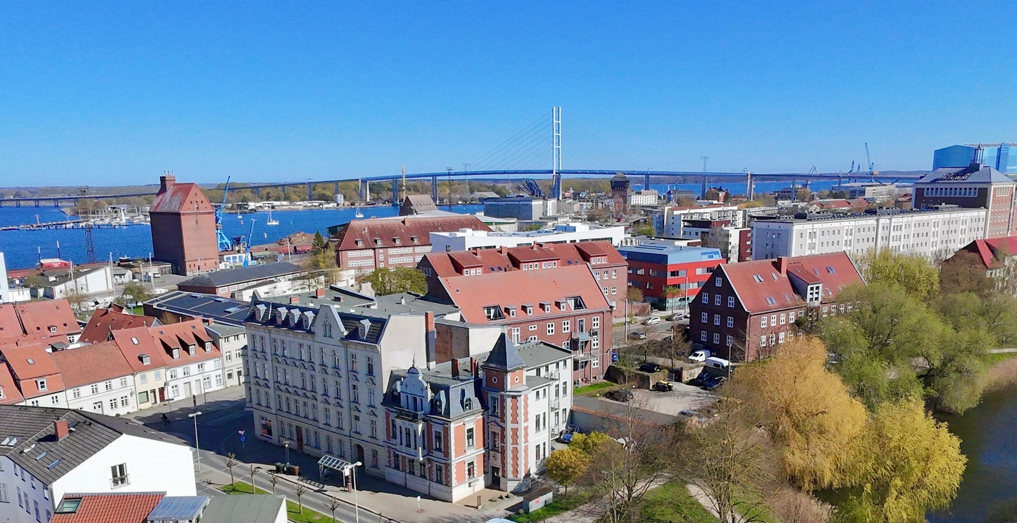 Eine Stadtansicht mit einer markanten Brücke, Gebäuden mit roten Dächern und einem Fluss.