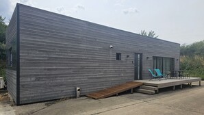 En moderne bygning med fladt tag, træterrasse og et lille udendørs opholdsområde med to stole og et bord.