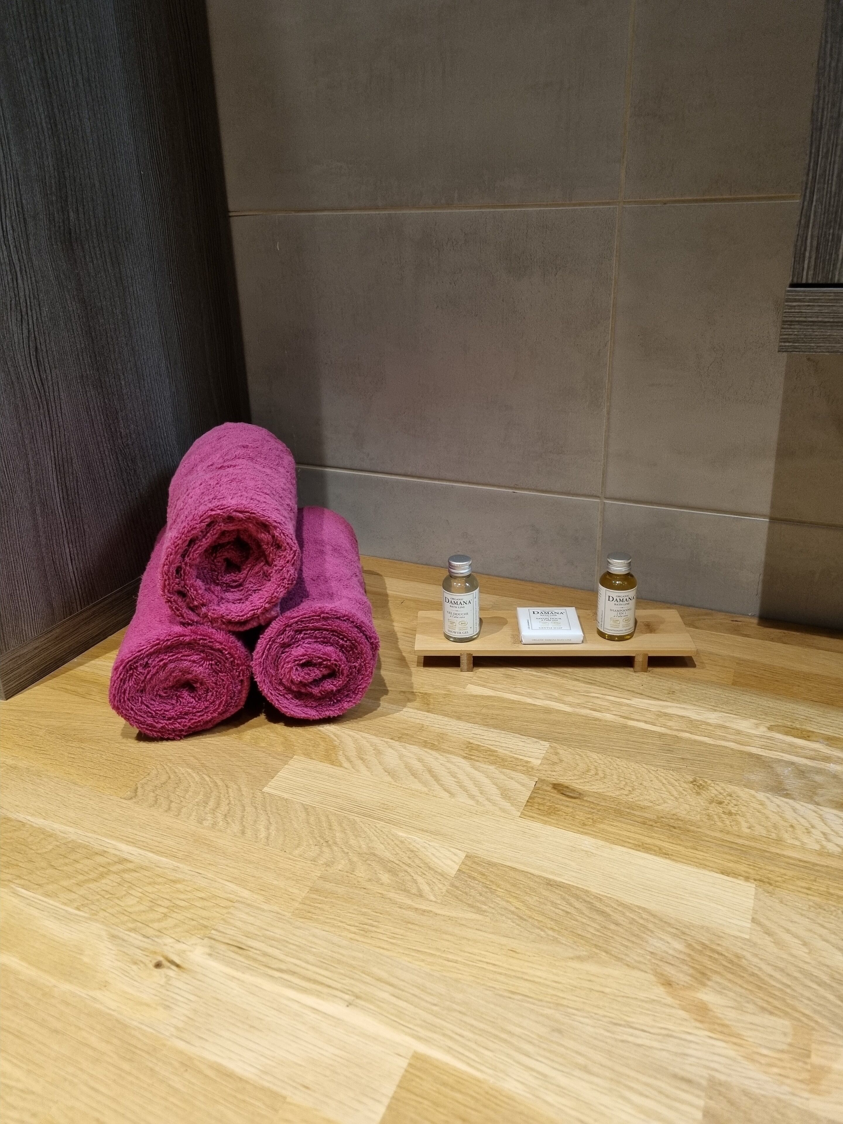 A wooden floor with a stack of rolled towels and two bottles on a small wooden shelf.