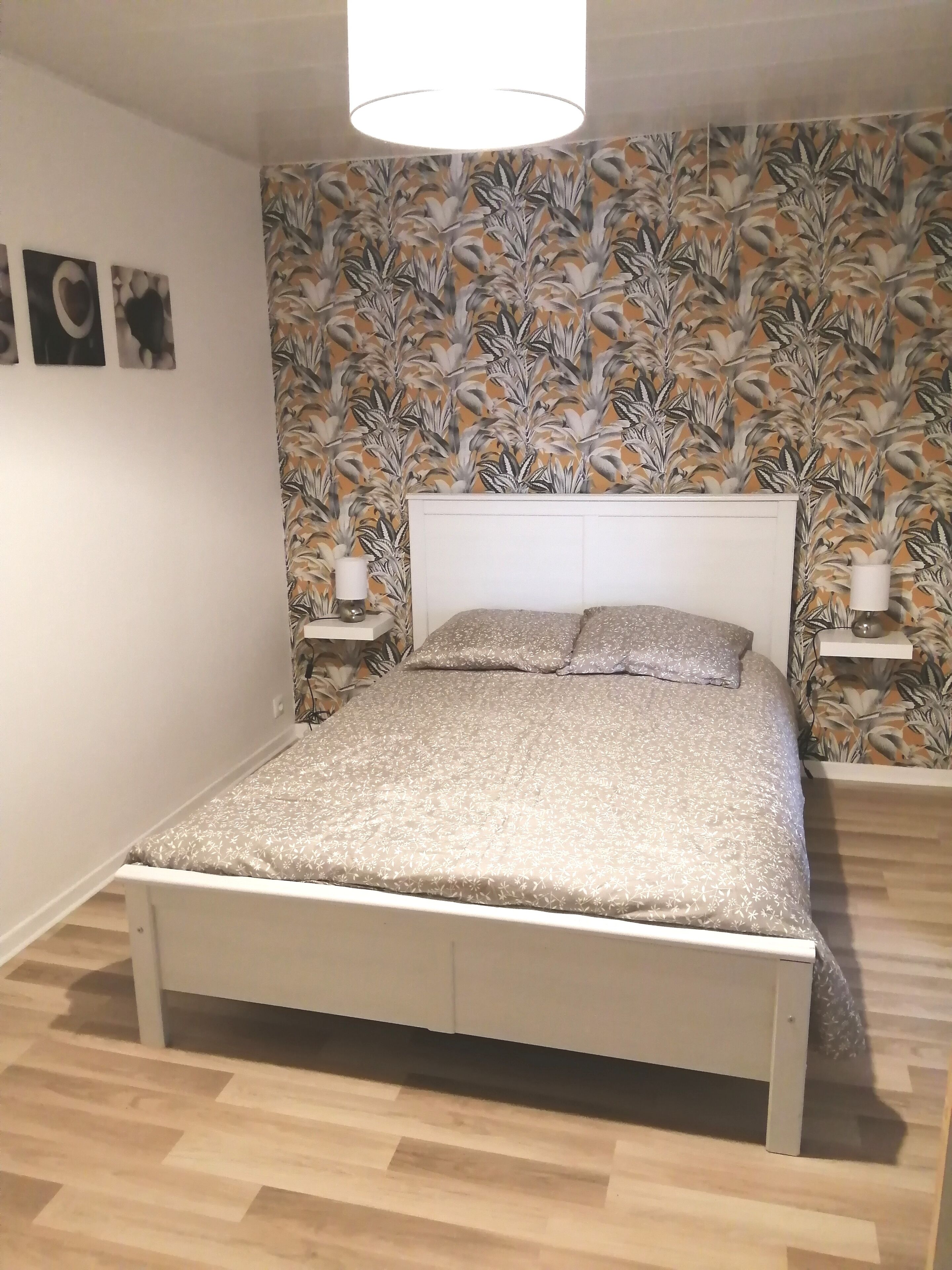 A bedroom with a bed, a wall with a floral wallpaper, and a ceiling light.