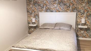 A bedroom with a bed, a wall with a floral wallpaper, and a ceiling light.