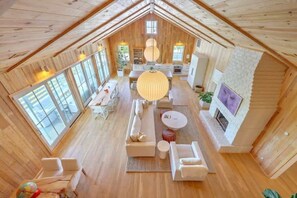 Amplio espacio tipo loft con techo alto, paredes de madera, chimenea y ventanas grandes.