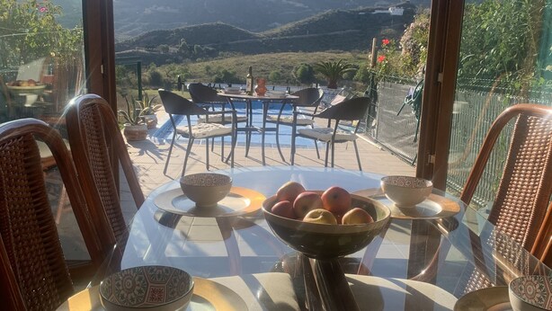 Un coin repas avec une table en verre, des chaises en osier et une vue sur les montagnes.