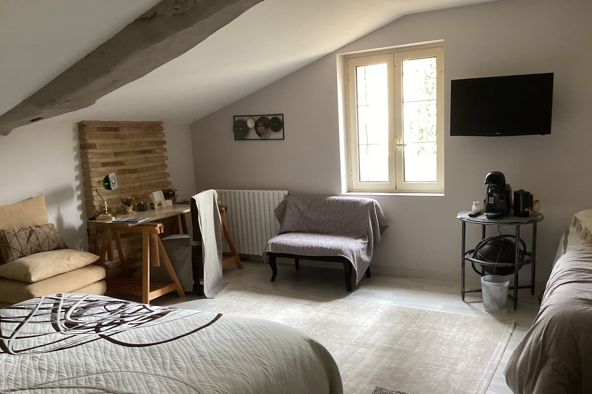 Une pièce confortable avec un plafond en pente, un radiateur, un bureau avec une lampe, une chaise, un lit et un téléviseur.