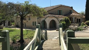 A wooden bridge leading to a stone building with arches and a tiled roof.