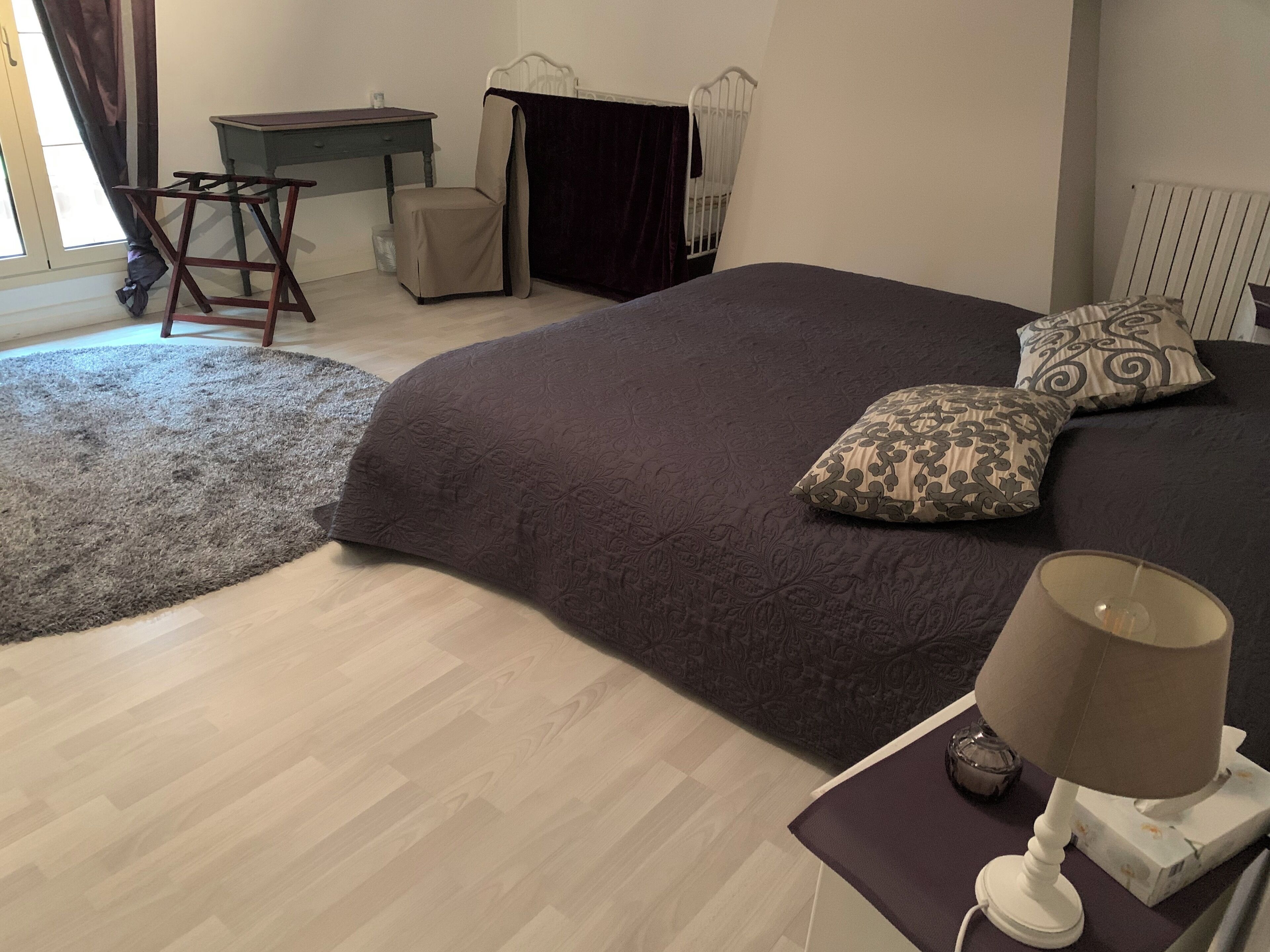 Un dormitorio con una cama grande, una mesita de noche con lámpara, una silla, un escritorio y un radiador.