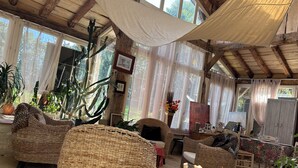 A spacious room with high ceilings, large windows, wicker furniture, and various plants.
