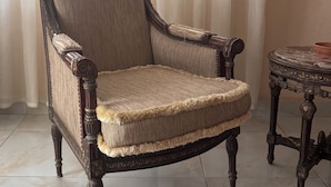 A chair with a high back and armrests, a table with a decorative top, and a window with a curtain. - Rino Residential apartment for families (Cairo Governorate)