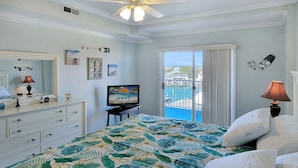 Een slaapkamer met een bed, een dressoir, een televisie en uitzicht op de oceaan door een schuifdeur.