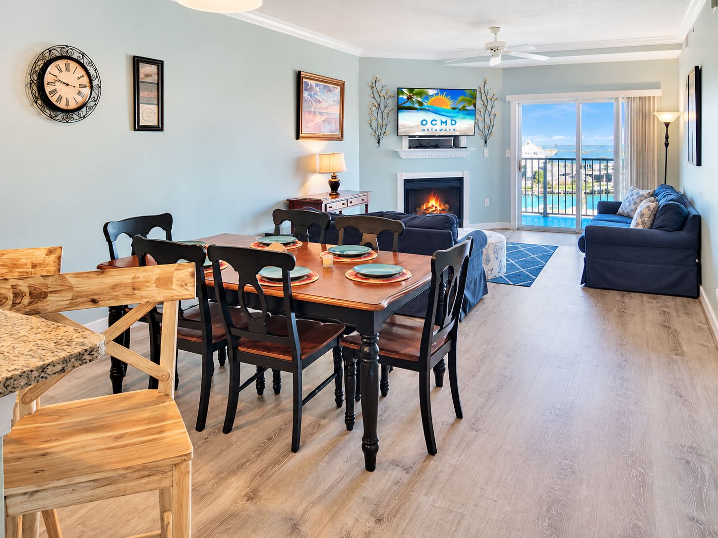 A dining area with a wooden table and chairs, a fireplace, and a television displaying 'OCMD GETAWAYS'.