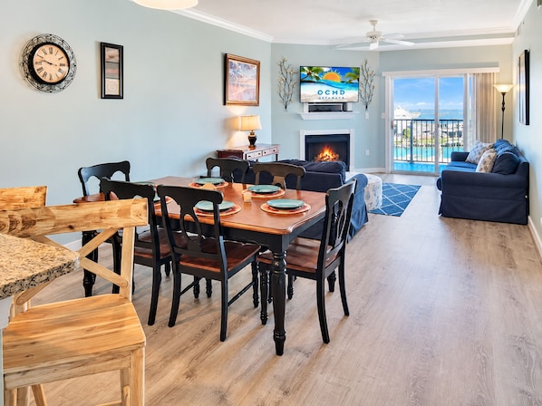 Un comedor con una mesa y sillas de madera, una chimenea y un televisor mostrando 'OCMD GETAWAYS'.