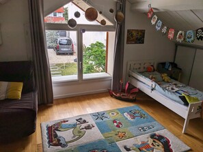 A room with a sofa, a bed, a window with a view of a car and greenery, and a wall with a pirate-themed banner. - Large house with swimming pool in Lyon ideal for families, close to transport links (Lyon)