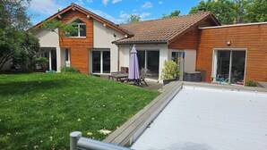 Una casa a due piani con facciata in legno, un patio con mobili da esterno e una piscina.