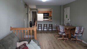 A living room with a grey sofa, a wooden dining table with four chairs, and a kitchen area with wooden cabinets and a microwave. - Seaworthy at Wheelhouse Lake Ozark MO (Lake Ozark)