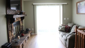 A living room with a stone fireplace, a sofa, and a large window with blinds. - Seaworthy at Wheelhouse Lake Ozark MO (Lake Ozark)