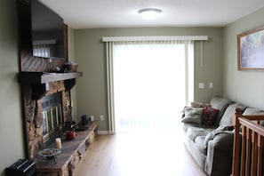 Una sala de estar con chimenea de piedra, un sofá y un ventanal con persianas.