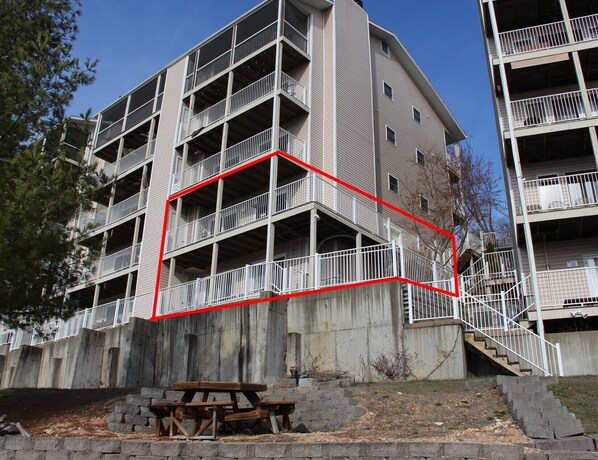 Un edificio de varios pisos con balcones, fachada de concreto y una mesa de picnic al frente.