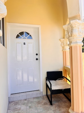 A white door with a window and a letter 'B' on it, a small bench with a cushion, and a tiled floor.