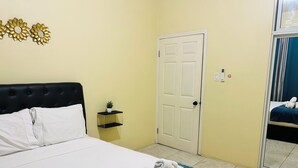 Habitación de hotel con cama, mesita de noche con planta, puerta y espejo que refleja la cama.