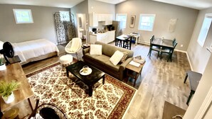 A spacious living area with a sofa, coffee table, and a dining table. There is a kitchenette in the background and a separate bedroom area. - TC TWO OAKS Studio / Downtown / Clean & Spacious (Traverse City)