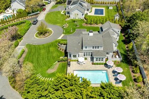 A residential property with a swimming pool, a driveway, and a well-maintained lawn.