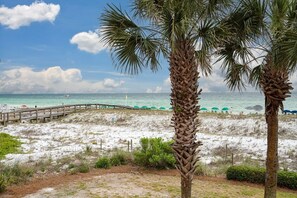 A beach with palm trees, a wooden walkway, and umbrellas. - Aegean 219 2 Bedroom Condo by RedAwning (Destin)