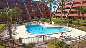 Ein Hotel mit Swimmingpool, umgeben von Palmen und Liegestühlen.