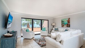 Ein Wohnzimmer mit großem Fenster, Flachbildfernseher, blauem Schrank und einer Sofagarnitur.