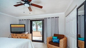 Ein Schlafzimmer mit einem Bett, einem Fernseher, einem Korbsessel und einem Balkon mit Blick auf Palmen.