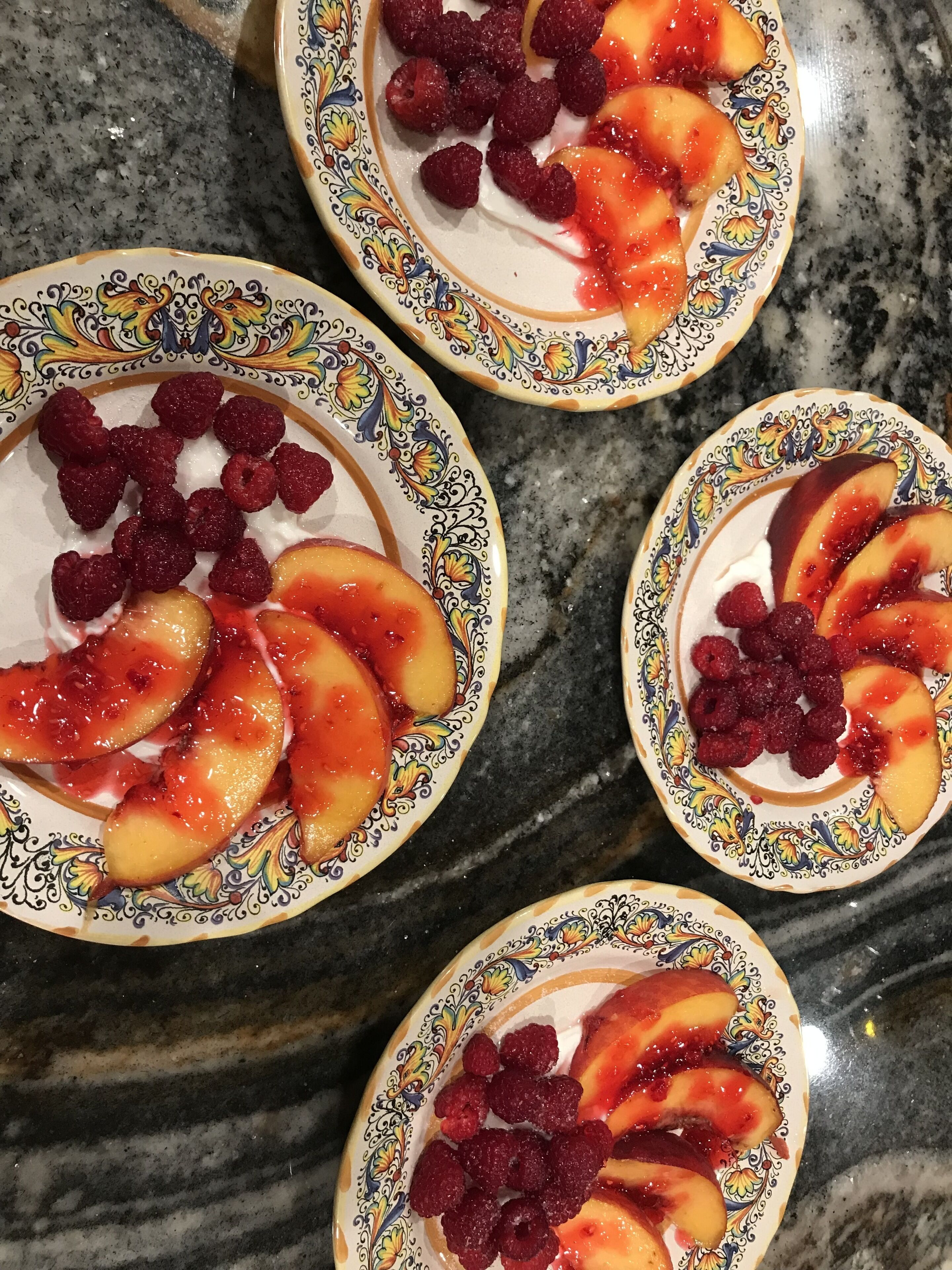 Cuatro ensaladas de frutas con frambuesas y melocotones sobre una encimera de mármol.