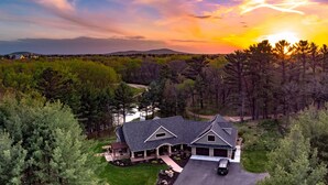A large house with a driveway, surrounded by dense trees and a lake.