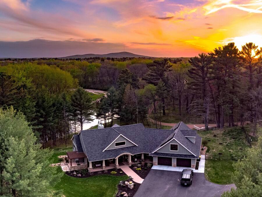 A large house with a driveway, surrounded by dense trees and a lake.