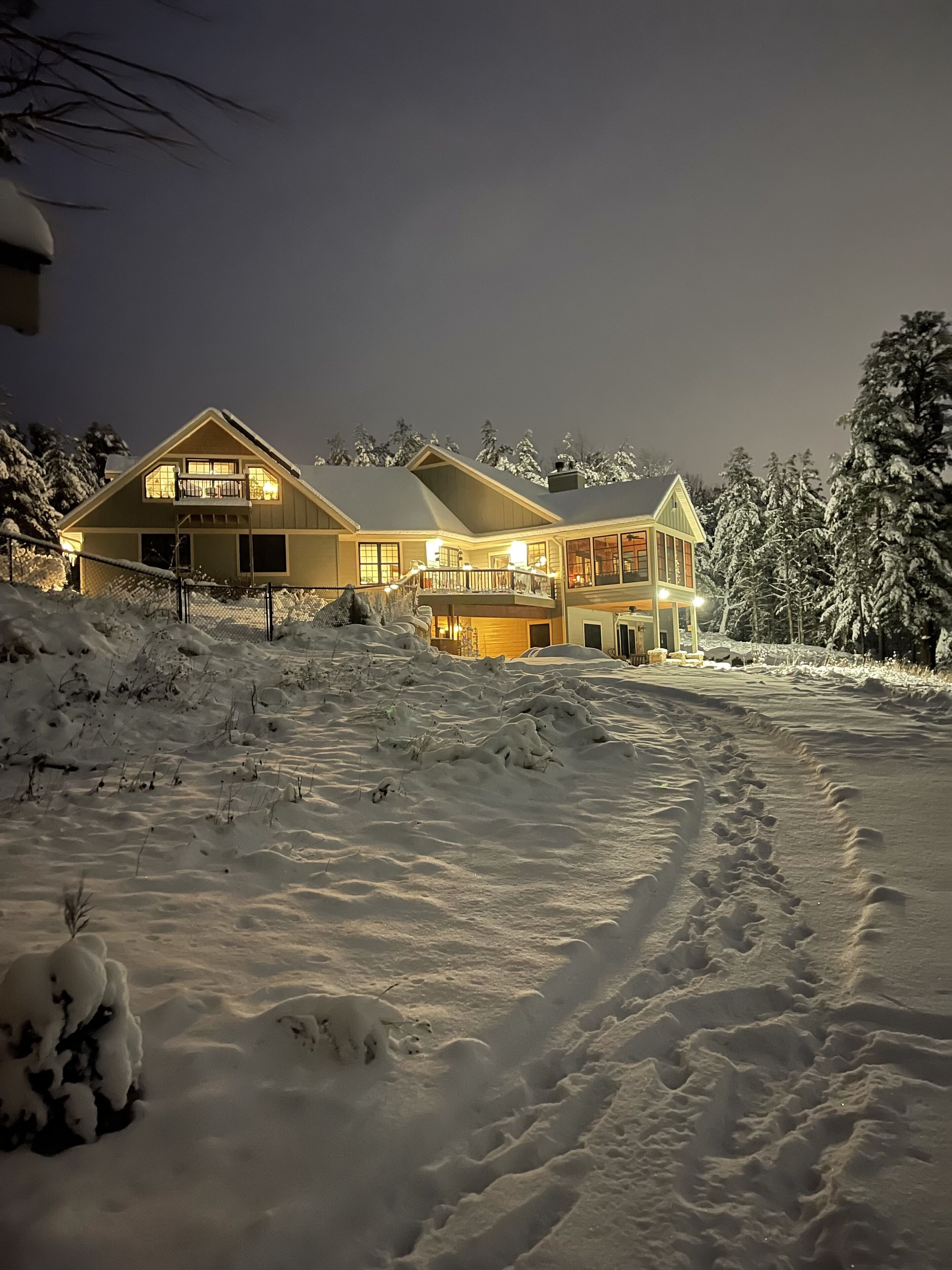 A large, two-story house with a balcony, surrounded by snow-covered trees and a snowy landscape.