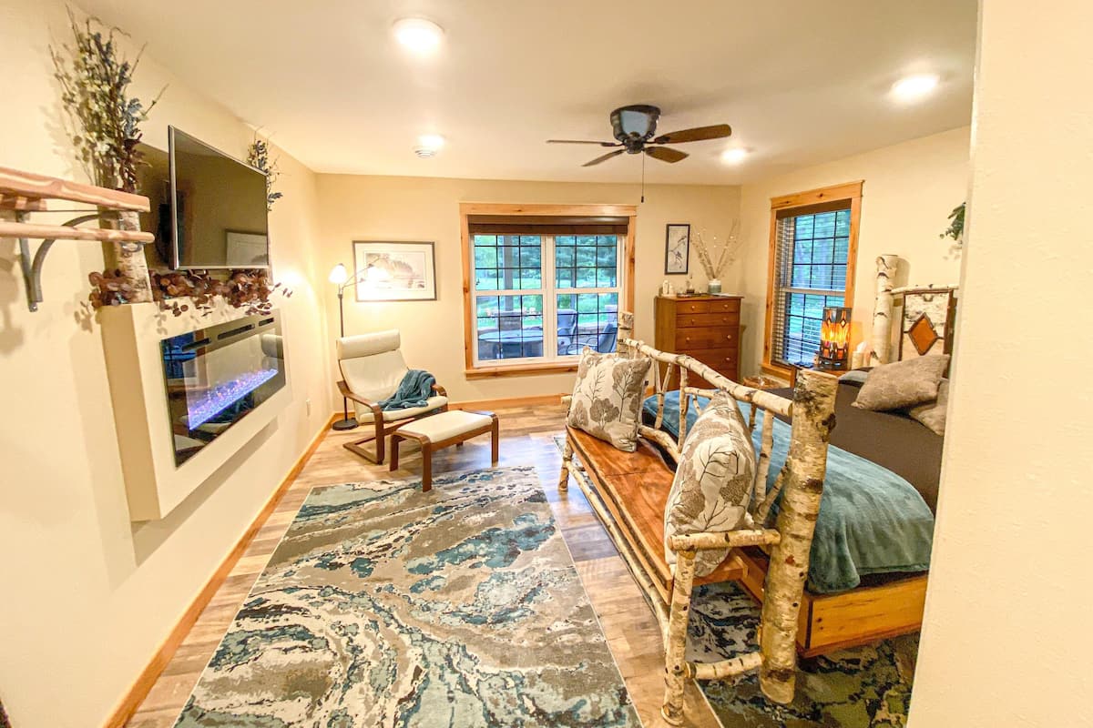 A living room with a fireplace, a television, a large window, and a ceiling fan.