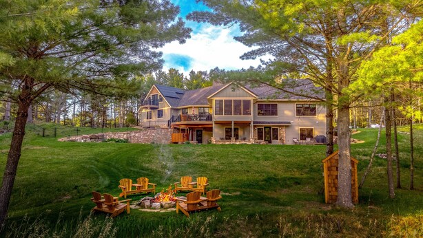 A large house with a fire pit and outdoor seating, surrounded by a well-maintained lawn and trees.
