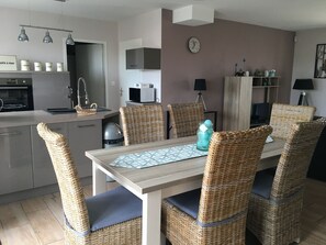 Een moderne keuken met een eethoek, voorzien van rieten stoelen en een tafel met een tafelkleed met geometrische patronen.